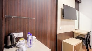 Habitación de hotel con un armario de madera, un pequeño escritorio con silla, un televisor de pantalla plana montado en la pared y un hervidor sobre la encimera.
