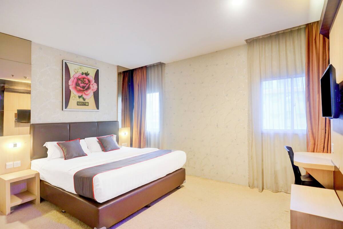 A hotel room with a large bed, bedside tables, a desk, a television, and curtains.