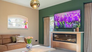 Een moderne woonkamer met een grote flatscreen televisie, een open haard, een bank en een salontafel met een bloevas.
