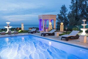 Un espace aménagé au bord de la piscine, avec des chaises longues, un belvédère décoratif et une vue sur l’océan.