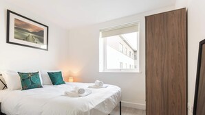 A bedroom with a bed, pillows, a framed picture, a window, and a wardrobe.