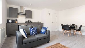 A modern living space with a grey sofa, a dining table with black chairs, and a kitchen area with grey cabinets and a microwave.