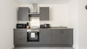 A modern kitchen with grey cabinets, a built-in oven, a microwave, and a coffee maker.