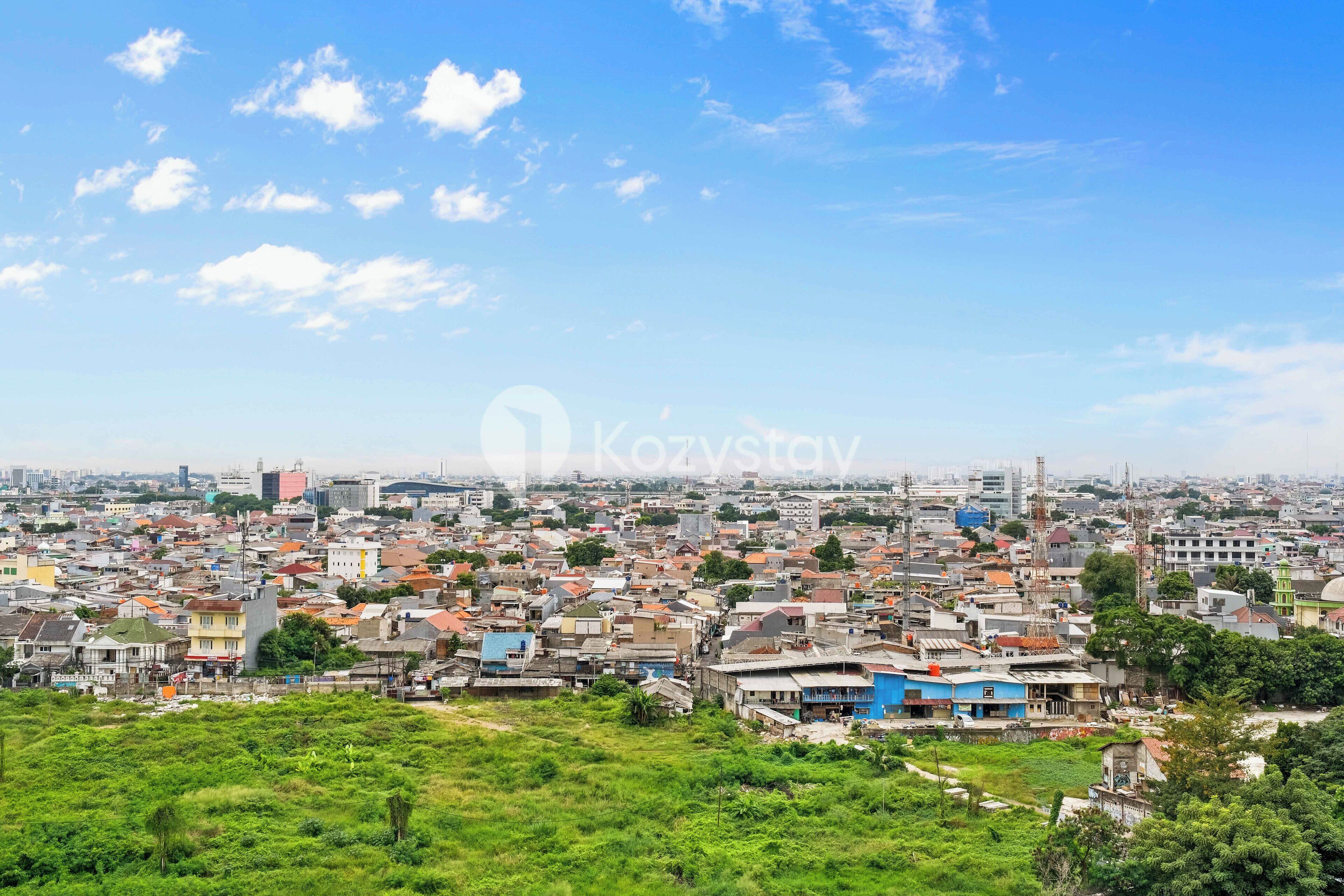 A densely populated urban area with a mix of residential and commercial buildings, a clear sky, and some greenery in the foreground.