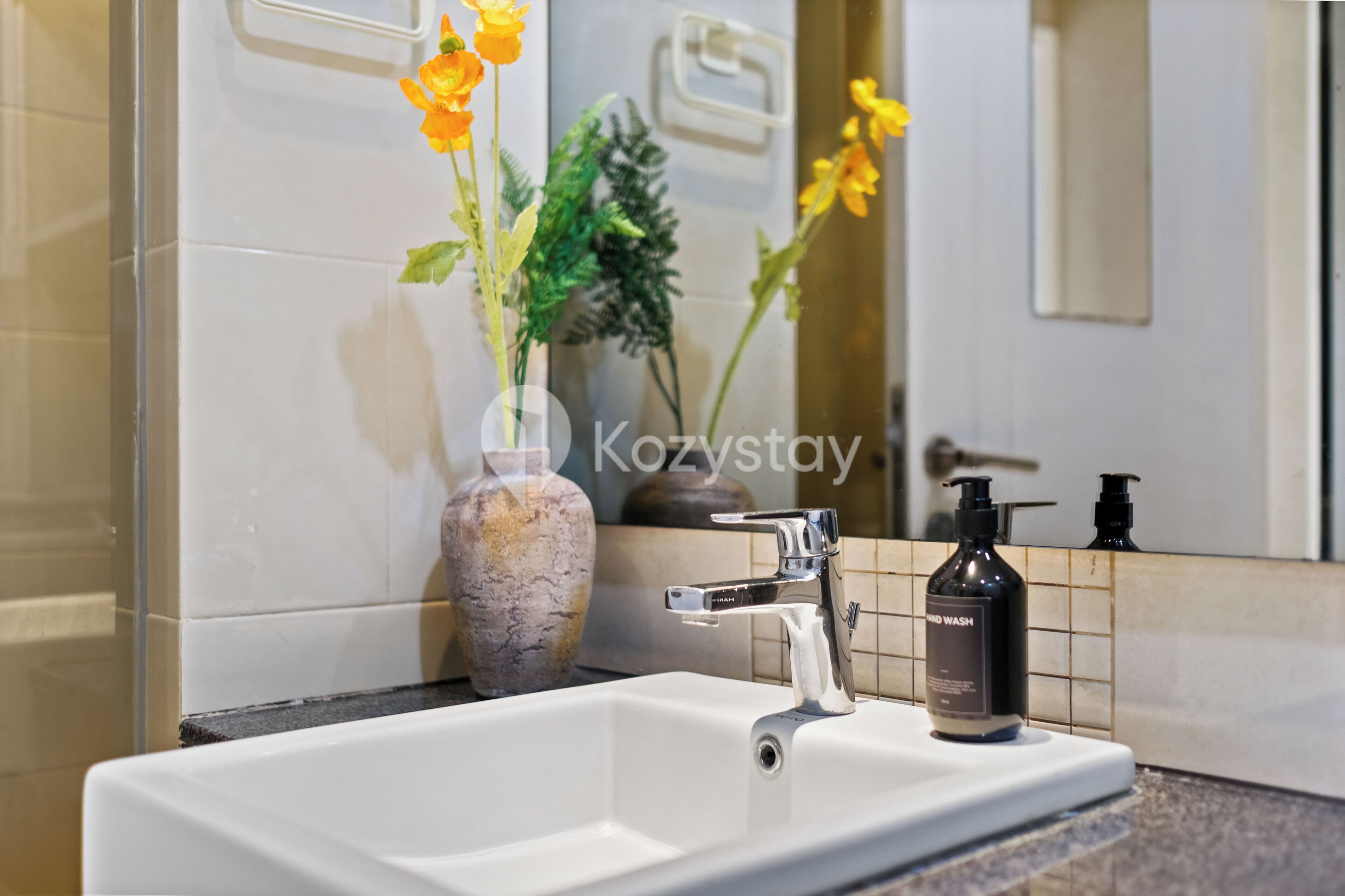 A bathroom with a white sink, a mirror, and a vase with flowers.