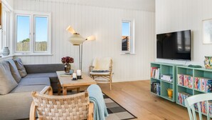 A cozy living room with a sofa, a chair, a table with candles, a floor lamp, a bookshelf, and a TV.