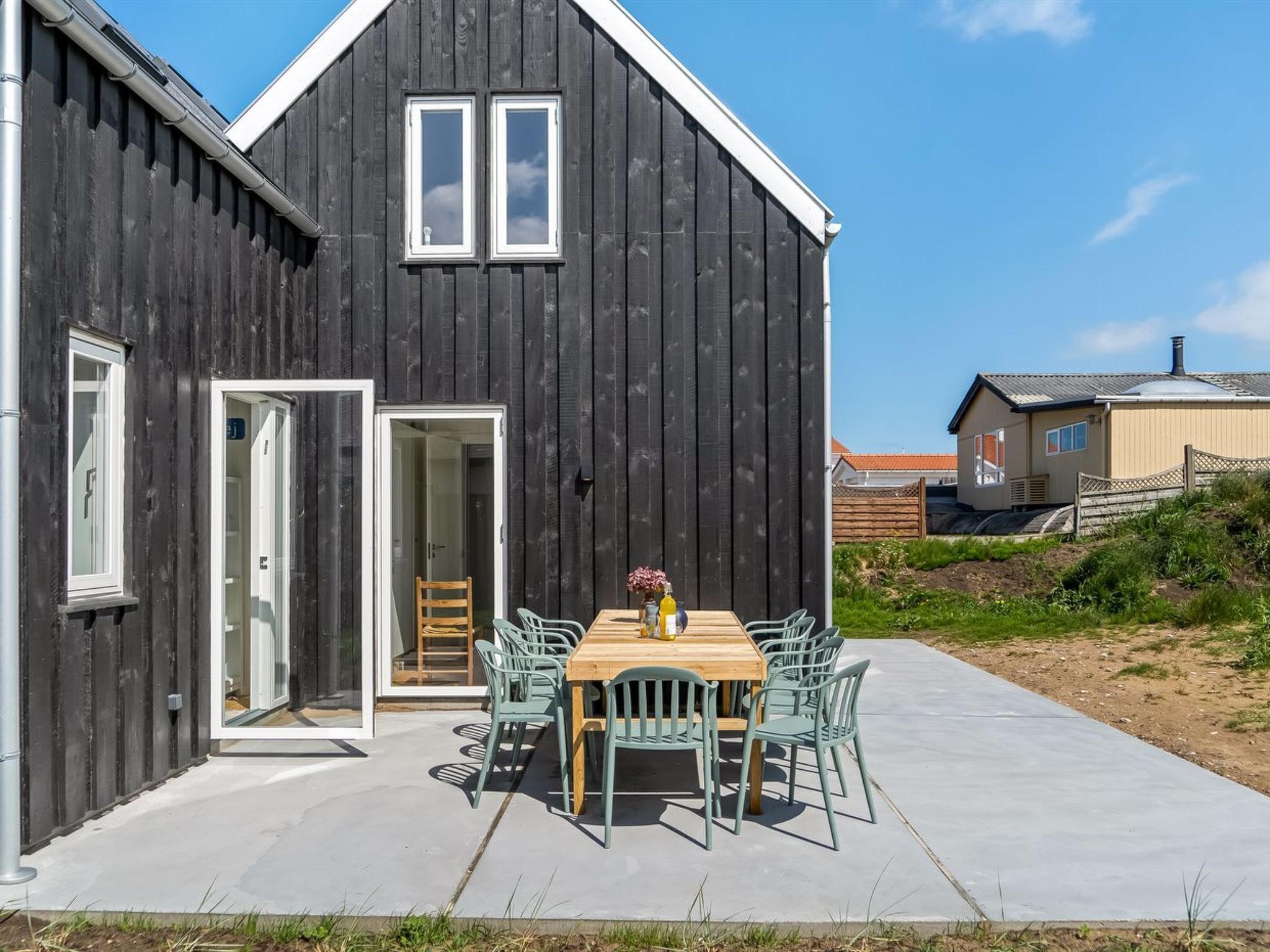 Ein modernes Haus mit einer großen Terrasse, einem Esstisch und Stühlen.