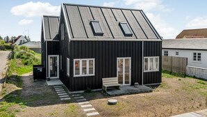 A modern black house with a sloped roof and skylights, a small porch, and a pathway leading to the entrance.