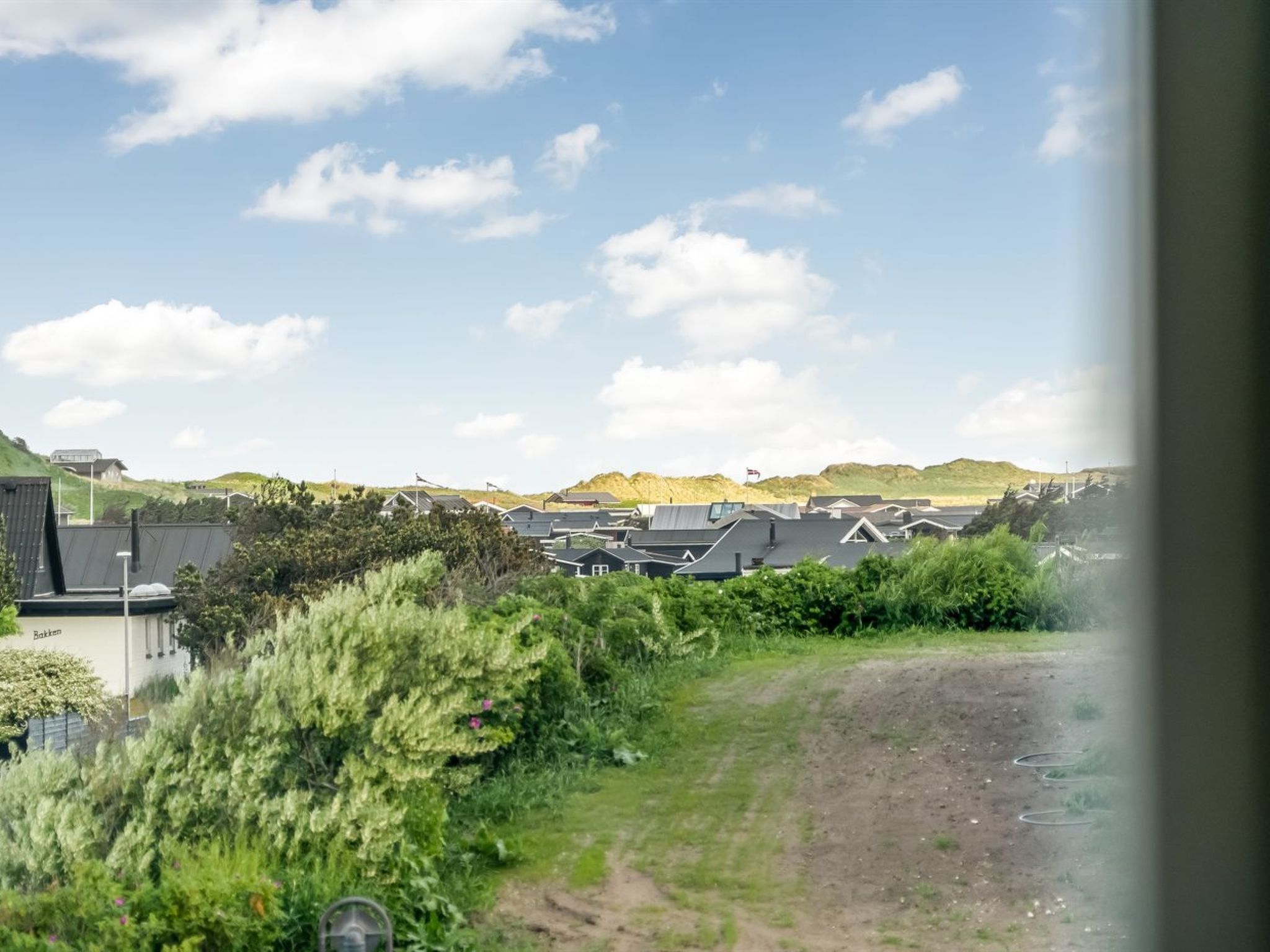 Un quartiere residenziale con case, un sentiero sterrato e una collina sullo sfondo.