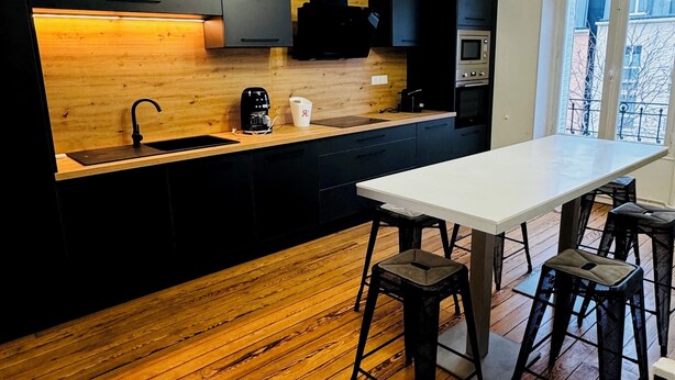 A modern kitchen with a wooden countertop, black cabinets, and a white dining table with stools.