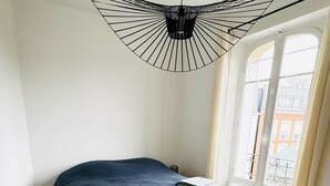 A bedroom with a bed, a white rug, wooden flooring, a window with a view, and a unique ceiling light fixture.