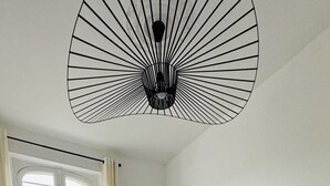 A bedroom with a large bed, a window with curtains, and a unique ceiling light fixture.
