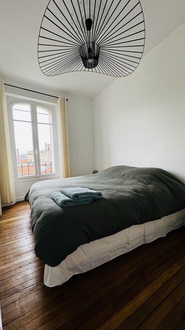 Un dormitorio con una cama grande, una ventana con cortinas y una lámpara de techo original.