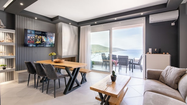 Una sala de estar moderna con una mesa de comedor de madera, sillas negras, un sofá gris y un televisor montado en la pared.