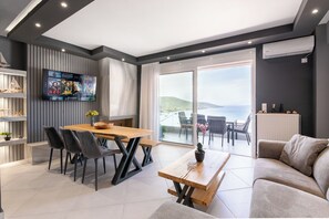 Una sala de estar moderna con una mesa de comedor de madera, sillas negras, un sofá gris y un televisor montado en la pared.