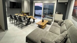 Una sala de estar moderna con un sofá gris, una mesa de comedor con sillas y un televisor montado en la pared.