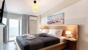 Una habitación de hotel moderna con una cama grande, una mesita de noche con lámpara, un cuadro sobre la cama y vistas al mar a través de una puerta corredera.