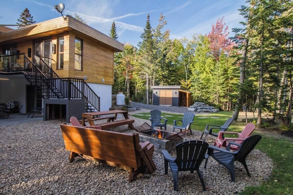 A cabin with a wooden exterior, a fire pit, outdoor seating, and a staircase leading to the upper level.