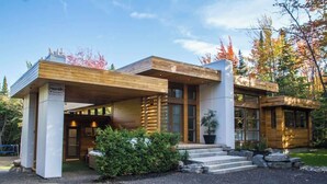 Een modern huis met twee verdiepingen, een overdekte veranda, grote ramen en een stenen fundering.