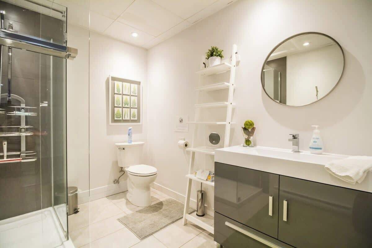 Ein modernes Badezimmer mit Duschkabine aus Glas, Toilette in Weiß, Waschbecken mit Spiegel und Ablage mit Pflanzen.