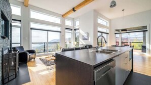 A modern kitchen with large windows, a central island, and a view of the outdoors.