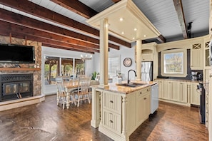 A spacious kitchen with a stone fireplace, wooden beams, and a large island with a sink.