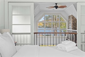 A bedroom with a large window, a ceiling fan, and a view of trees and a lake.