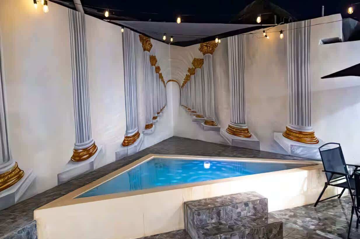 A swimming pool with white columns and gold accents, surrounded by stone steps and a chair.