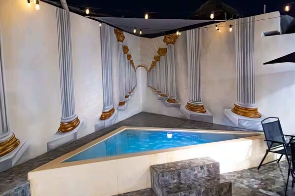 A swimming pool with white columns and gold accents, surrounded by stone steps and a chair.