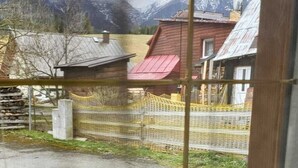 Uitzicht door een raam met houten kader, toont een landelijke omgeving met huizen, een hek en een berg op de achtergrond.