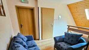 Een kamer met twee banken, houten vloeren, een schuine balkenkap en twee deuren.
