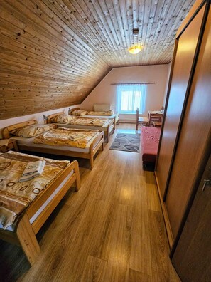 A cozy attic bedroom with wooden walls and floors, featuring three wooden beds with matching headboards, a small table, and a chair. - Penzión Ždiar (Ždiar)