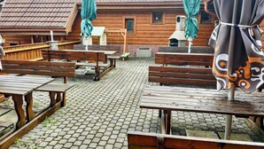 Een rustiek houten gebouw met een pannendak, buiten zitplaatsen met banken en tafels, en een terras met stenen bestrating.