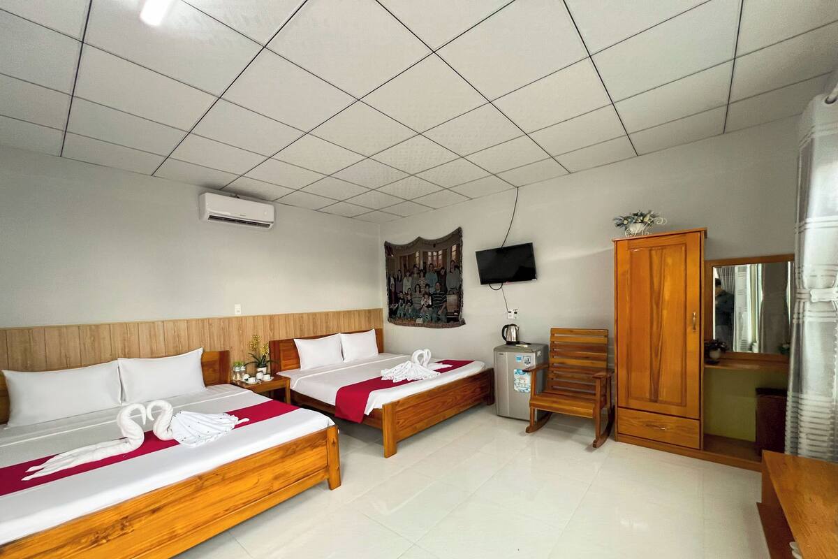Una habitación de hotel con dos camas de madera, una silla pequeña de madera, un televisor y un armario.