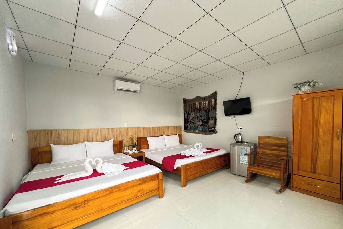 Habitación de hotel con dos camas de madera, un televisor montado en la pared, un armario de madera y una mesita con un hervidor.