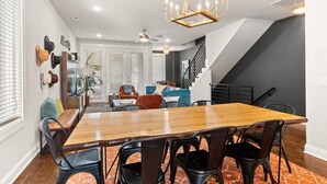 A dining area with a wooden table and chairs, a chandelier, and a staircase leading to another level.