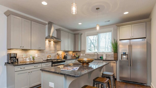 A modern kitchen with grey cabinets, a stainless steel refrigerator, and a central island with stools.