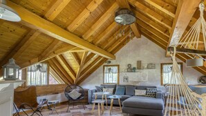 Un cuarto ático acogedor con techo de madera, un sofá, una silla y una hamaca colgante.