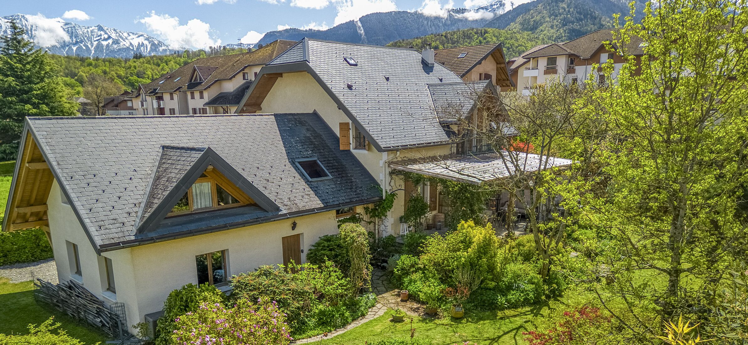 Une maison moderne dotée d’un toit en pente, entourée d’une végétation luxuriante et s’ouvrant sur un paysage montagneux.