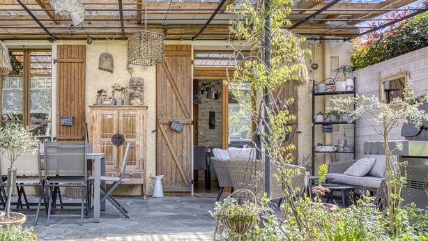 Un patio al aire libre con mobiliario rústico, una puerta de madera y diversas plantas en macetas.