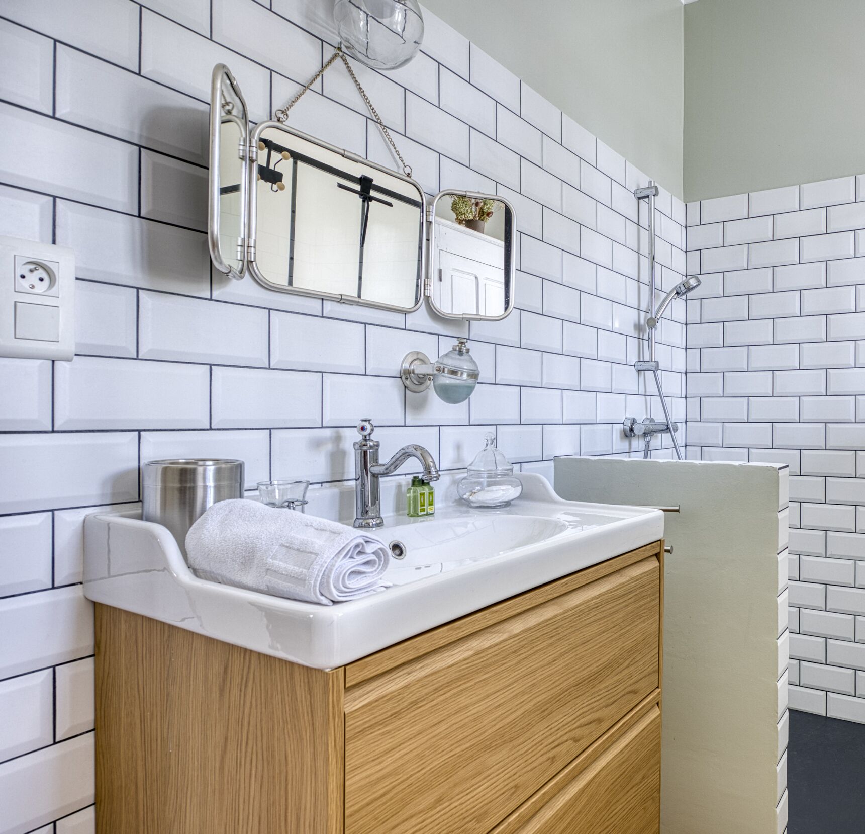 A modern bathroom with white subway tiles, a double sink vanity, wooden cabinetry, and a mirror with a glass enclosure.