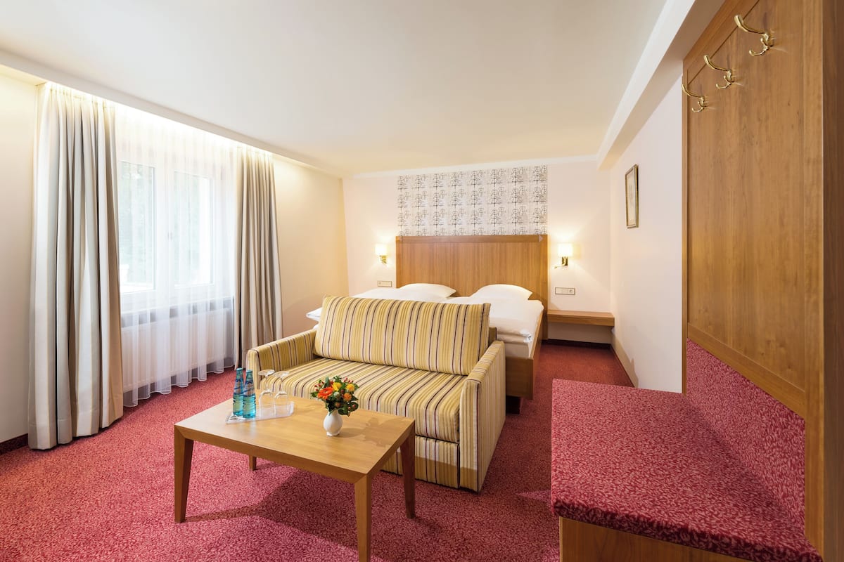A hotel room with a bed, a sofa, a wooden table, and a red carpet.