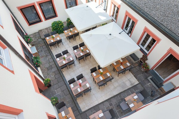 An outdoor patio with multiple tables and chairs, surrounded by buildings with red-framed windows. - Hotel Bayerischer Hof (Freising)