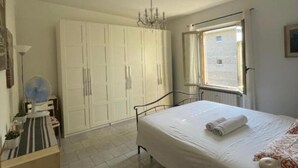 A bedroom with a bed, a wardrobe, a radiator, a window, and a fan.