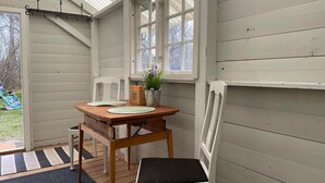 A small, enclosed porch with a wooden table and two chairs, a potted plant, and a window with white shutters. - 1 bedroom gorgeous home in Romakloster (Romakloster)
