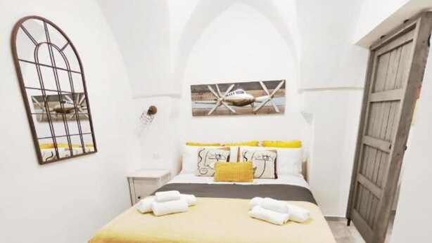 Un dormitorio con cama, mesita de noche, espejo y puerta de madera.