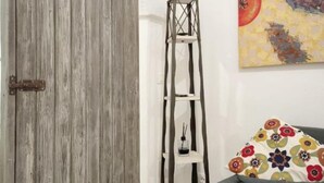 Una habitación con un armario de madera, una estantería blanca escalonada, un cuadro de colores y un sofá gris.