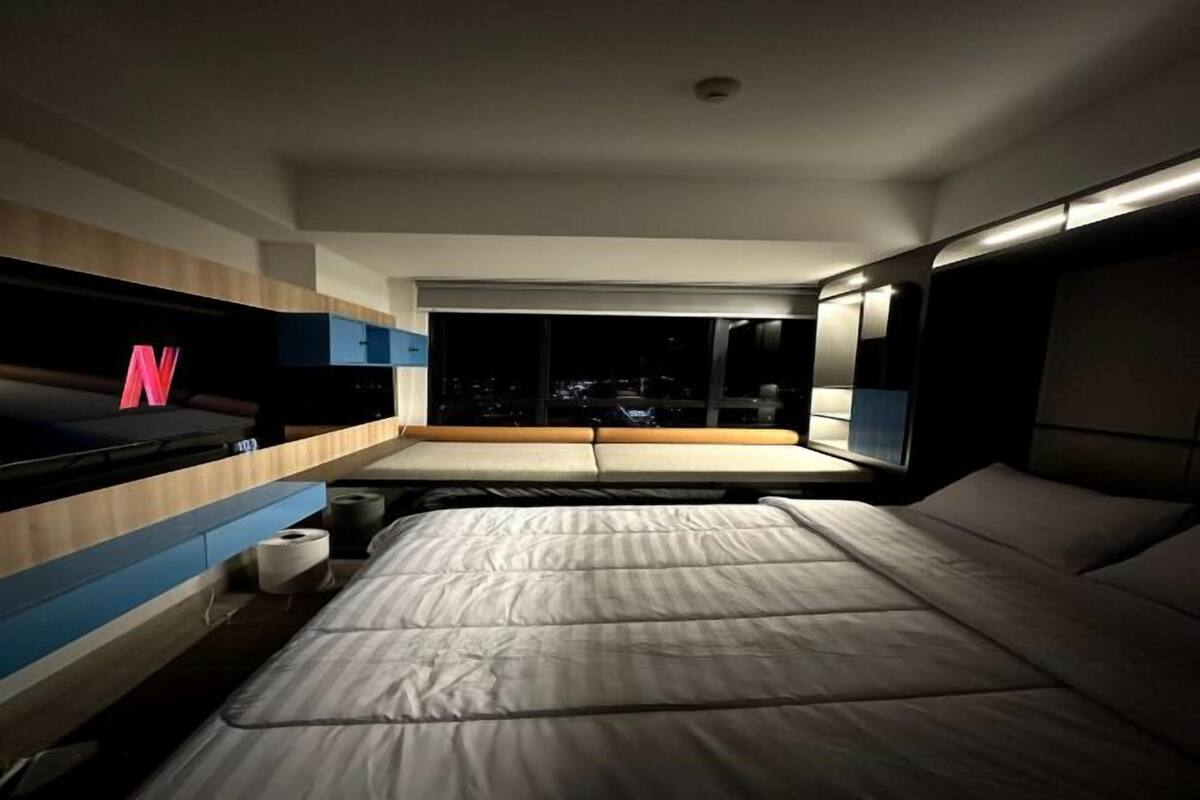 Un dormitorio moderno con cama, televisor y ventana con vistas a la ciudad.