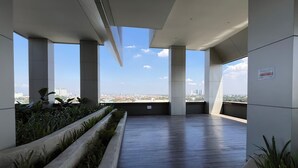 Una terraza moderna en la azotea con vistas al horizonte de la ciudad, que presenta un largo macetero estrecho con follaje y un piso de madera oscura y lisa.