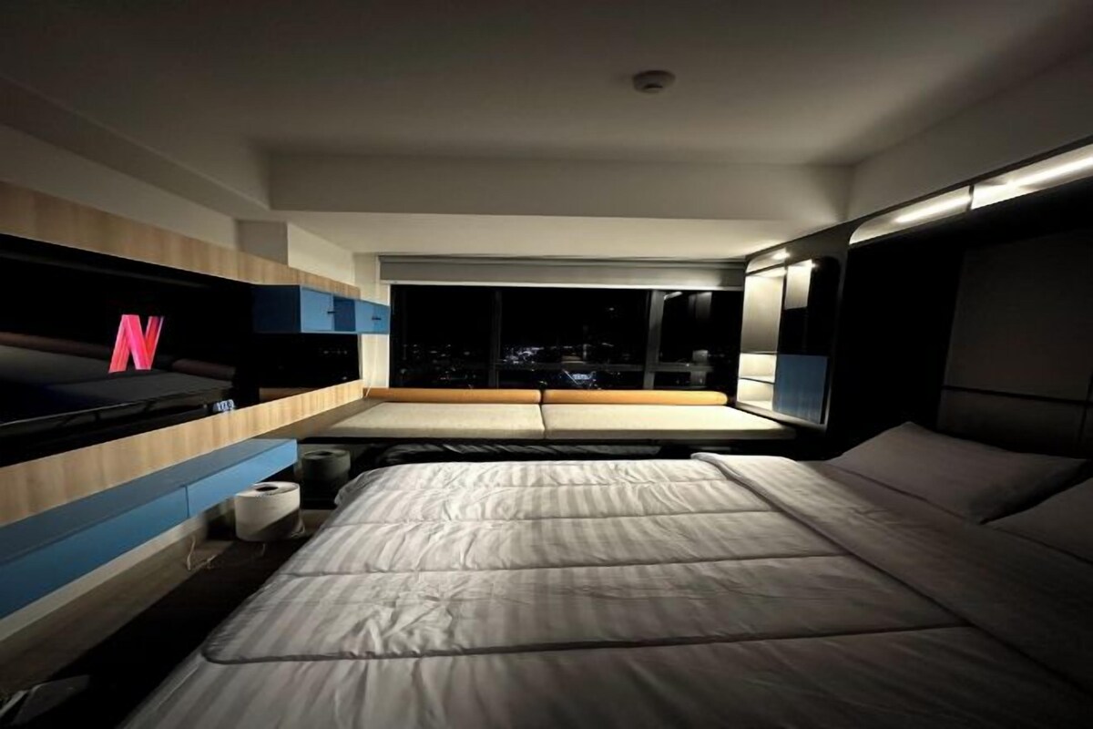 Una camera da letto moderna con un letto, una TV e una finestra con vista sulla città.